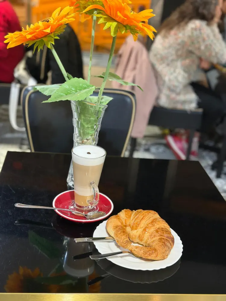 latte vaso alto con croisant en mesa y florero